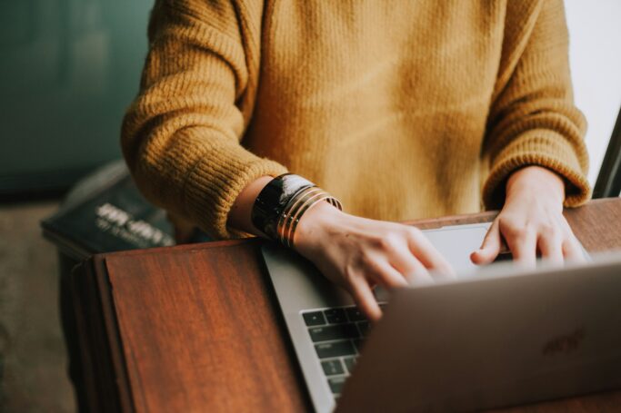 Person med orange tröja sitter framför en laptop